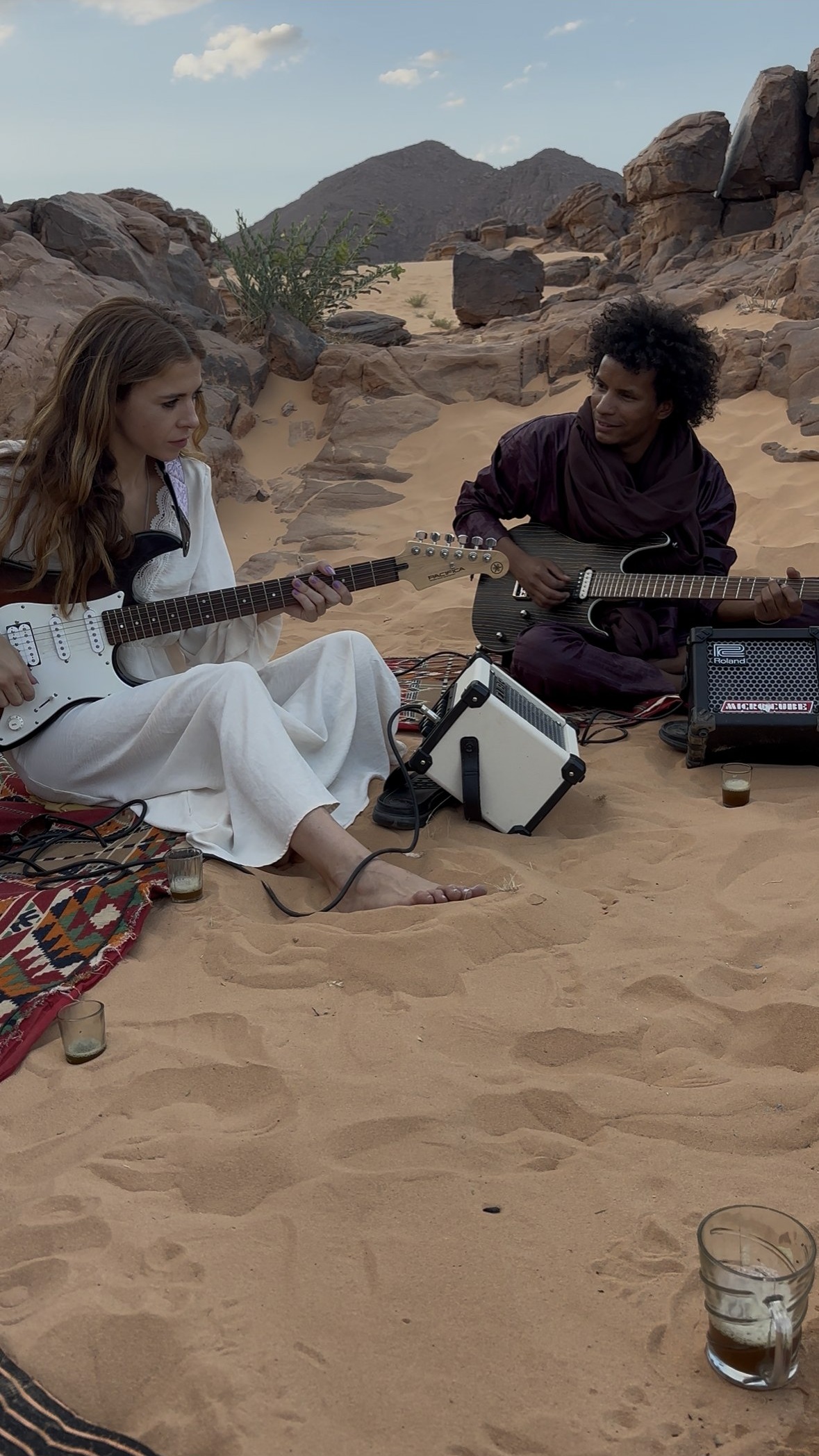 Mar Sánchez y Khily Ag Osman tocando guitarra eléctrica sentados en la arena, entre las rocas del Tassili n'Ajjer, Djanet